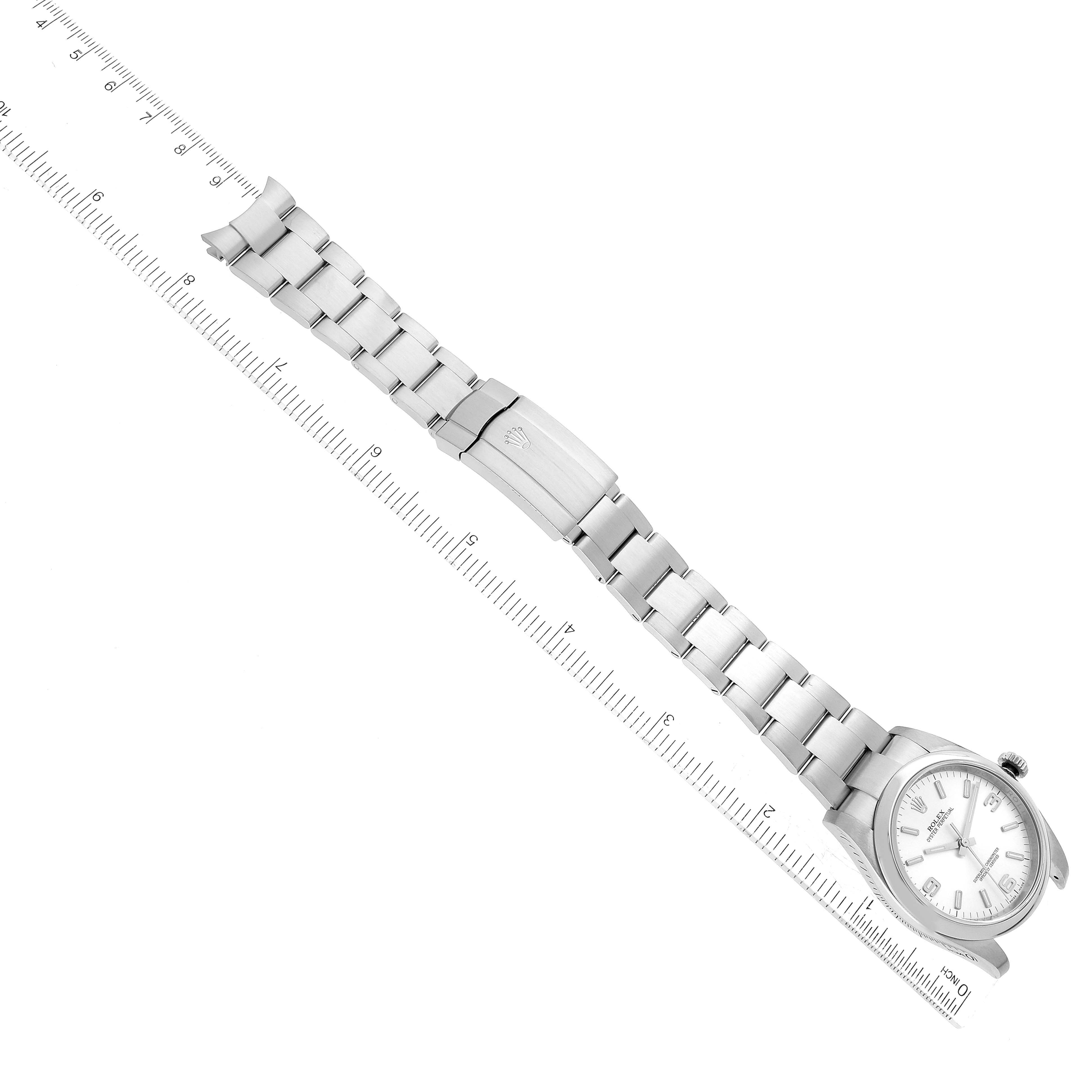The image shows a top-down view of the Rolex Oyster Perpetual 116000 Men
s Stainless Steel Silver Dial 116000 Men
s Stainless Steel Silver Dial watch, highlighting its face, bracelet, and clasp next to a ruler for scale.