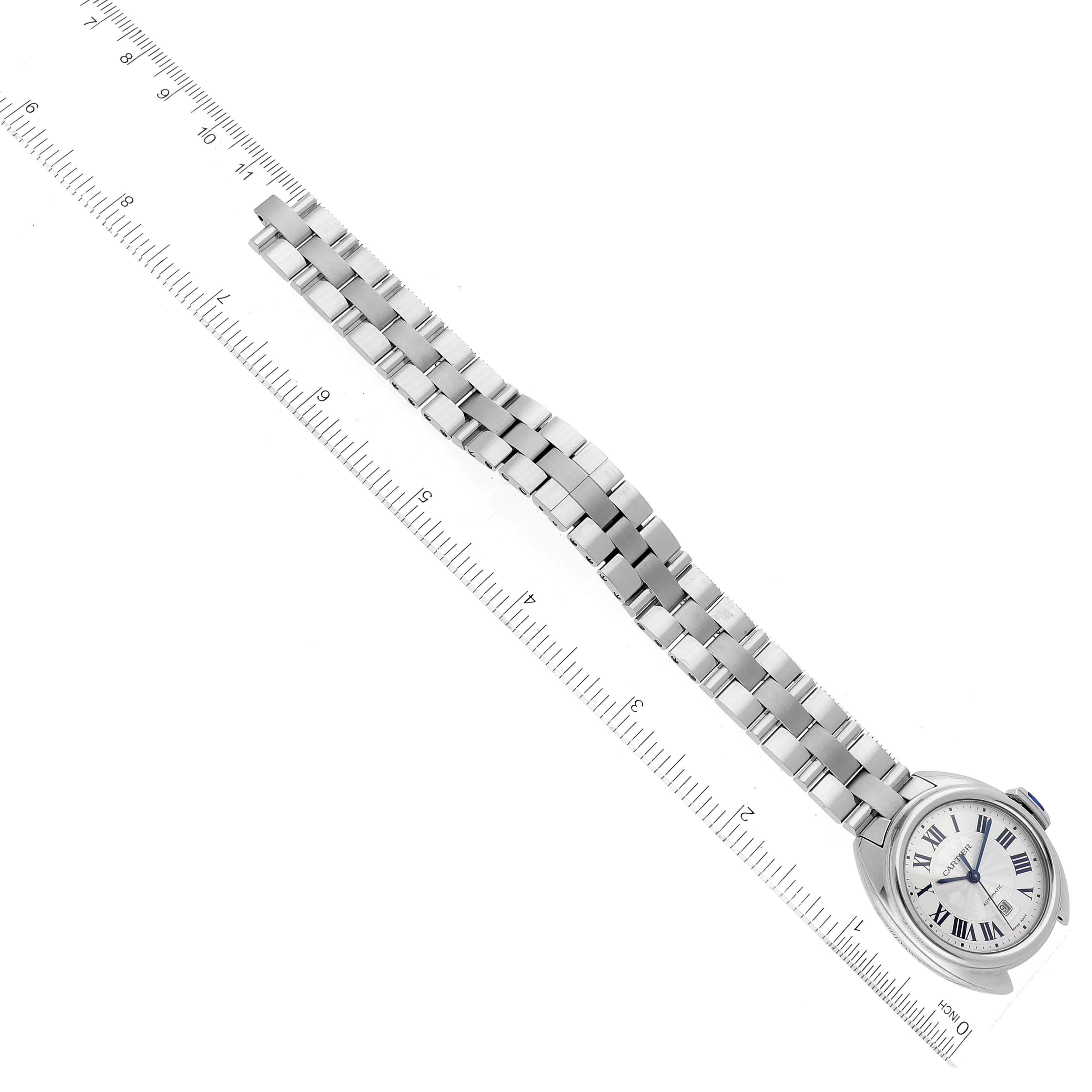 This Cartier Clé watch is shown from an angled top-down view, featuring its face and metal link strap alongside a ruler.