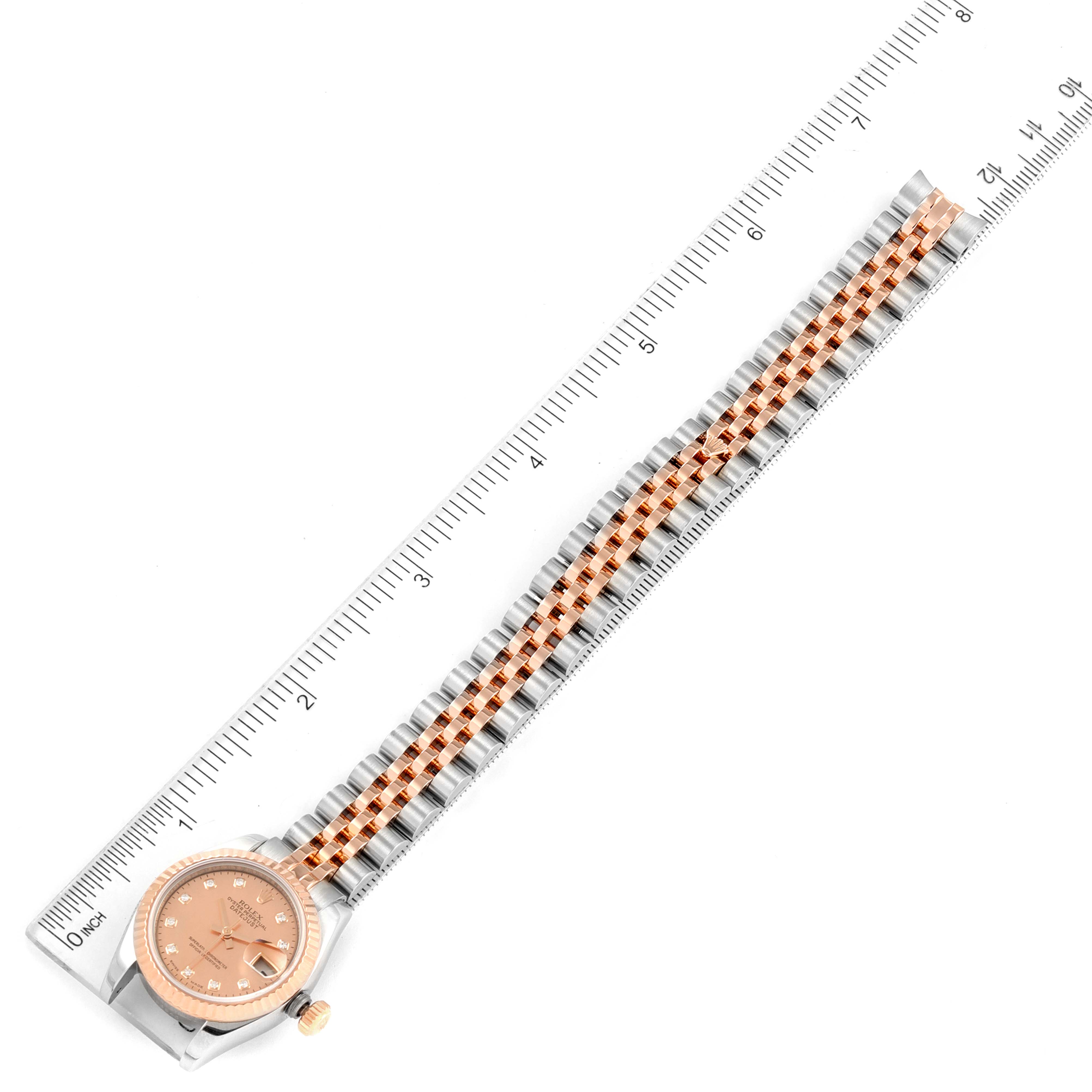 The image shows a Rolex Datejust 179171 Women's Steel and Gold (two tone) Mother of Pearl Dial 179171 Women's Steel and Gold (two tone) Mother of Pearl Dial watch with a pink dial and two-tone metal bracelet laid next to a ruler.