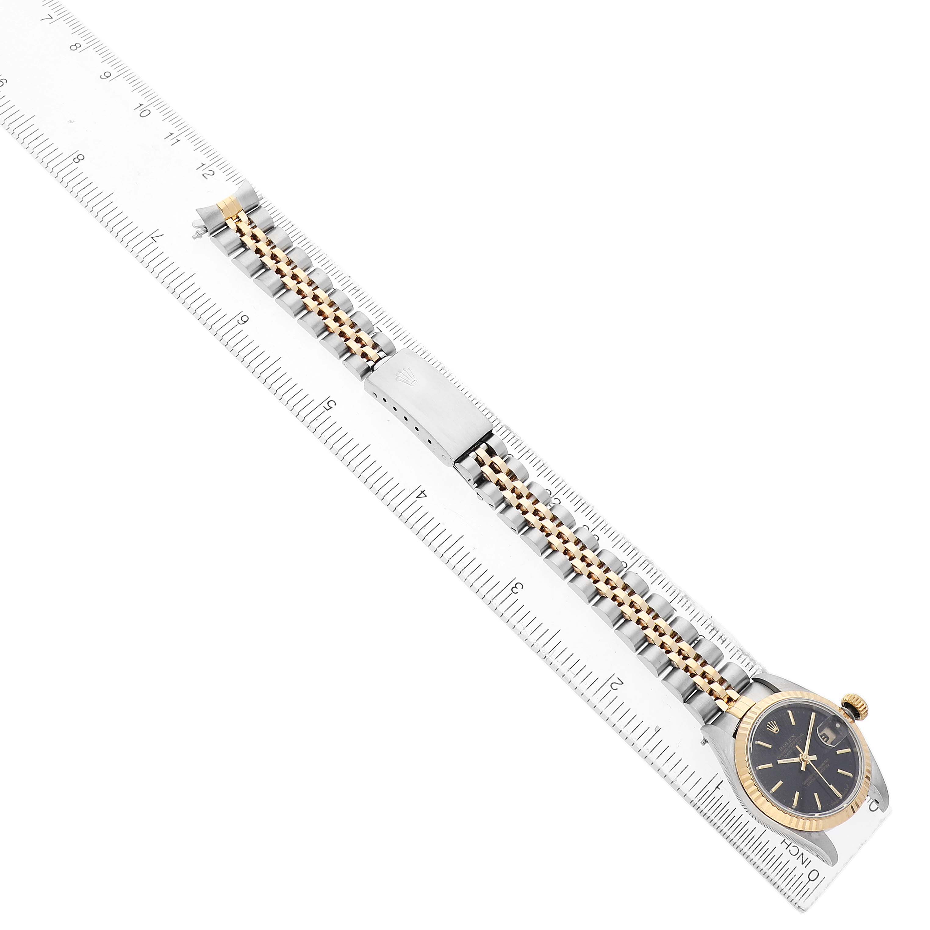 The Rolex Datejust 69173 Women's Steel and Gold (two tone) Black Dial watch is shown from a top view, displaying the face, bezel, bracelet, and clasp alongside a ruler for scale.