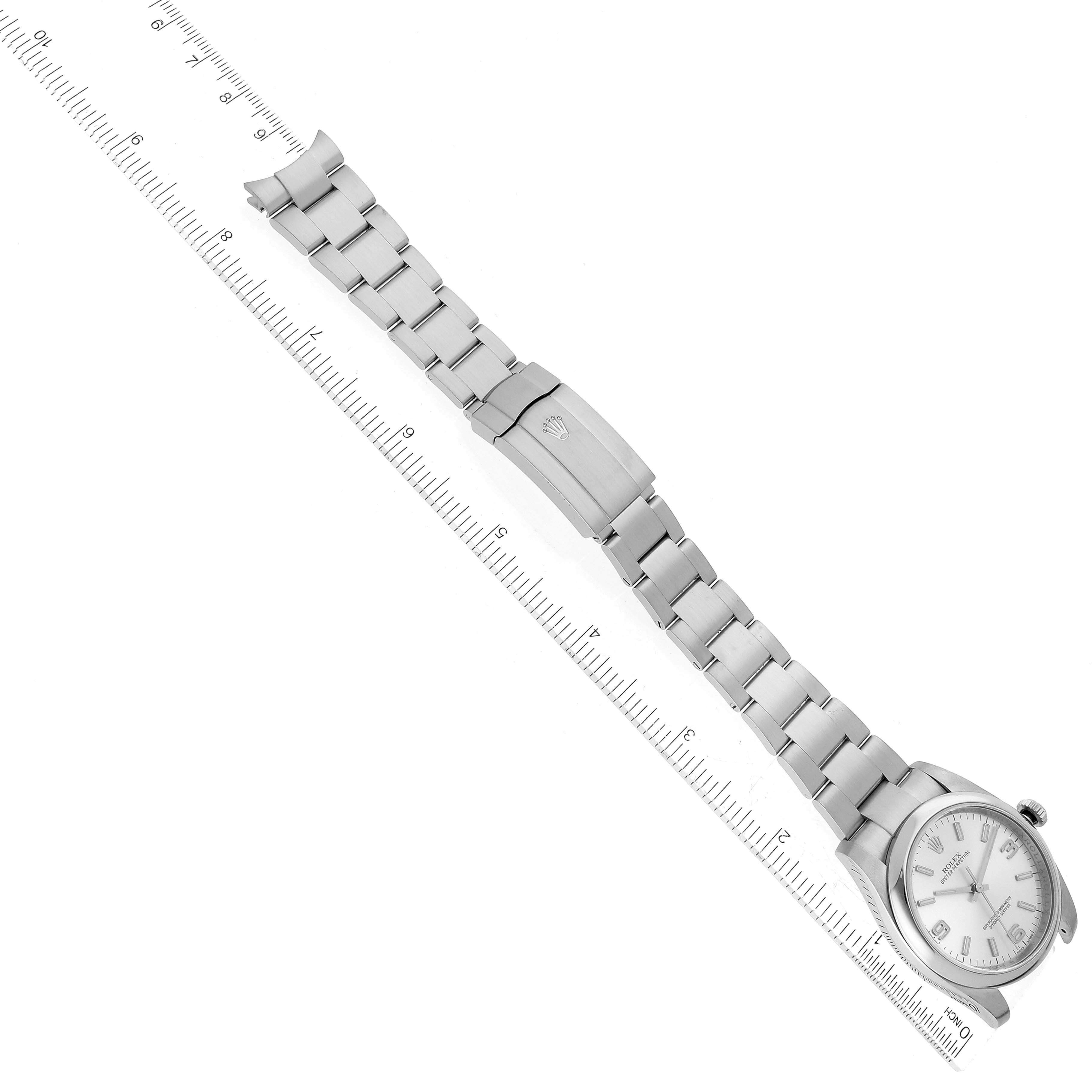 The image shows a Rolex Oyster Perpetual 116000 Men
s Stainless Steel Silver Dial 116000 Men
s Stainless Steel Silver Dial watch laid flat, showcasing its face and metal bracelet clasp, with a ruler for scale.