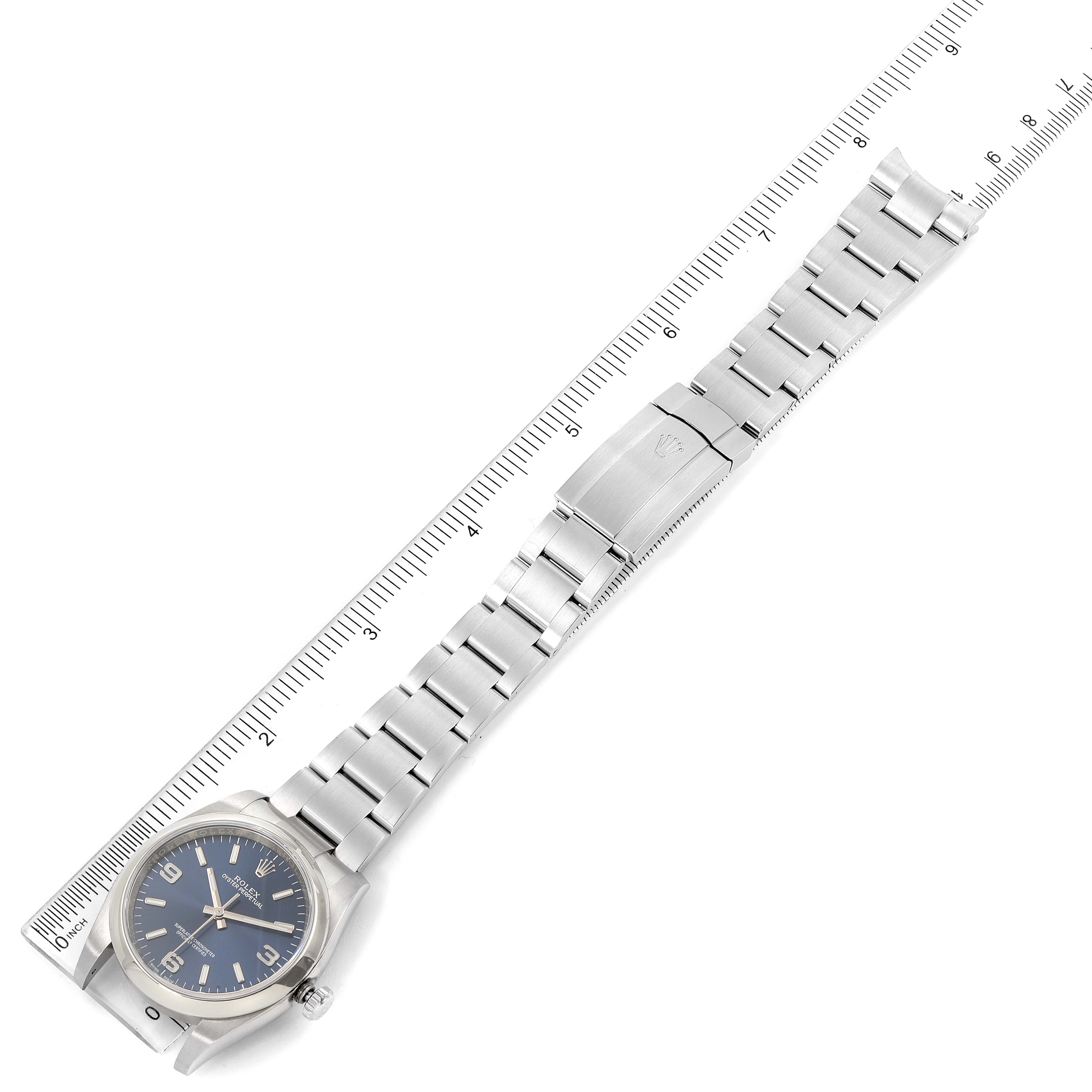 The image shows the entire Rolex Oyster Perpetual 116000 Men's Stainless Steel Blue Dial 116000 Men's Stainless Steel Blue Dial watch placed adjacent to a ruler, displaying the watch face, band, and clasp.