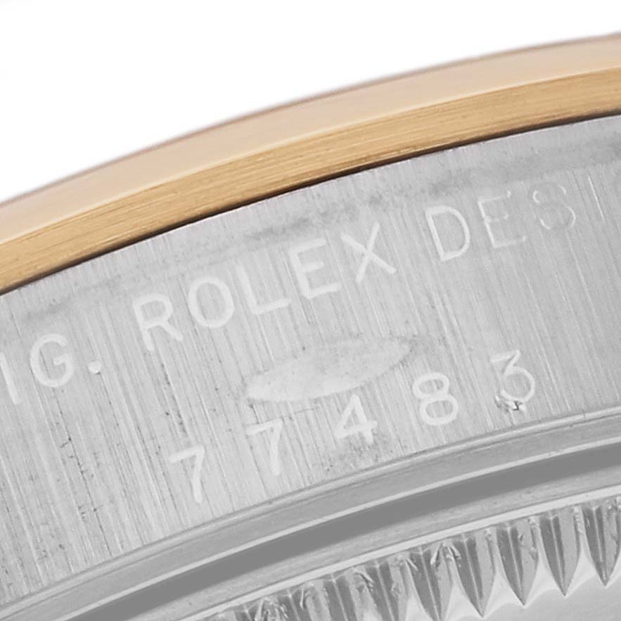 A close-up view of the edge of a Mid-Size Rolex watch, showing part of the bezel and engraved serial number on the case.