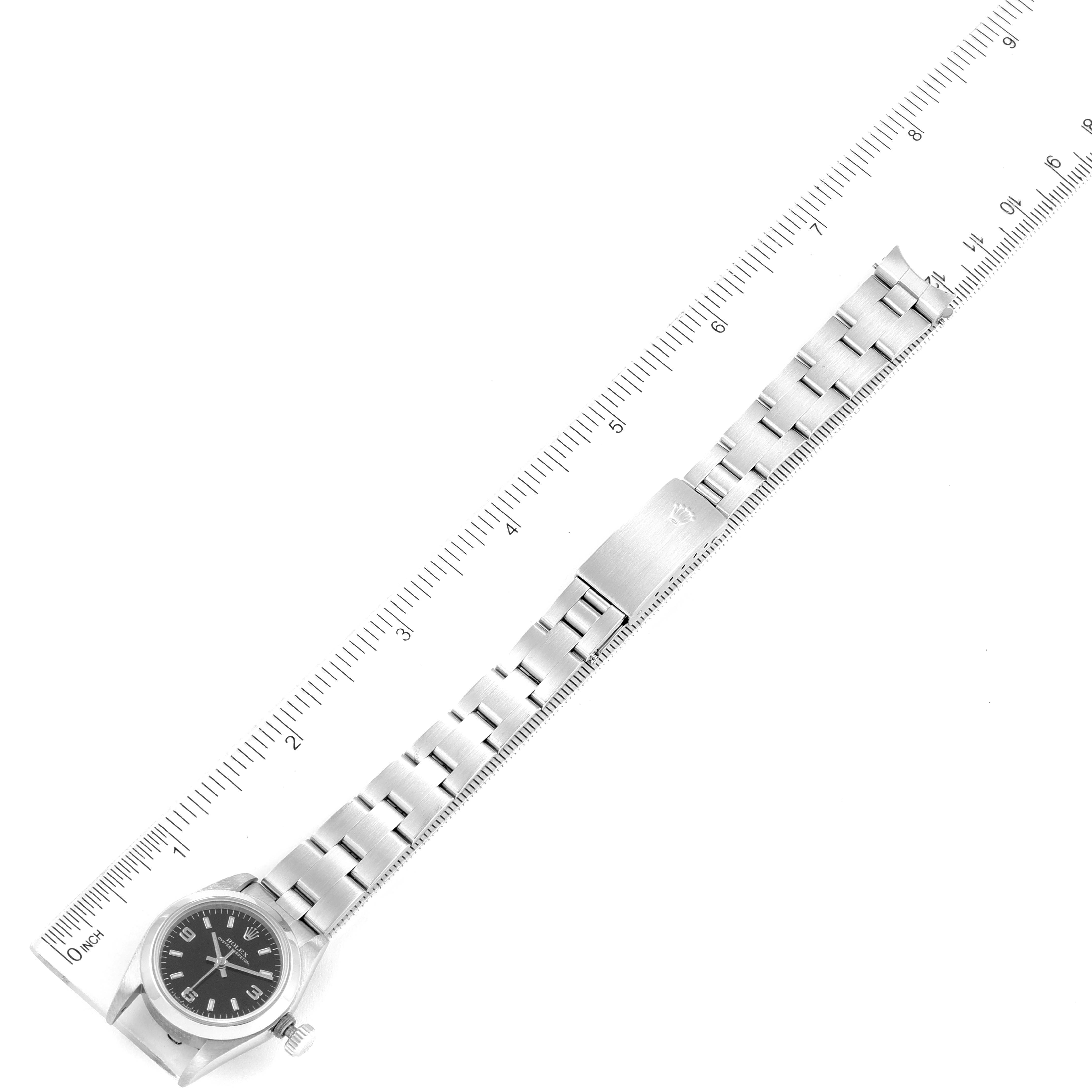 The image shows a side view of a Rolex Oyster Perpetual 67180 Women
s Stainless Steel Black Dial 67180 Women
s Stainless Steel Black Dial watch with its bracelet fully extended next to a measuring scale.