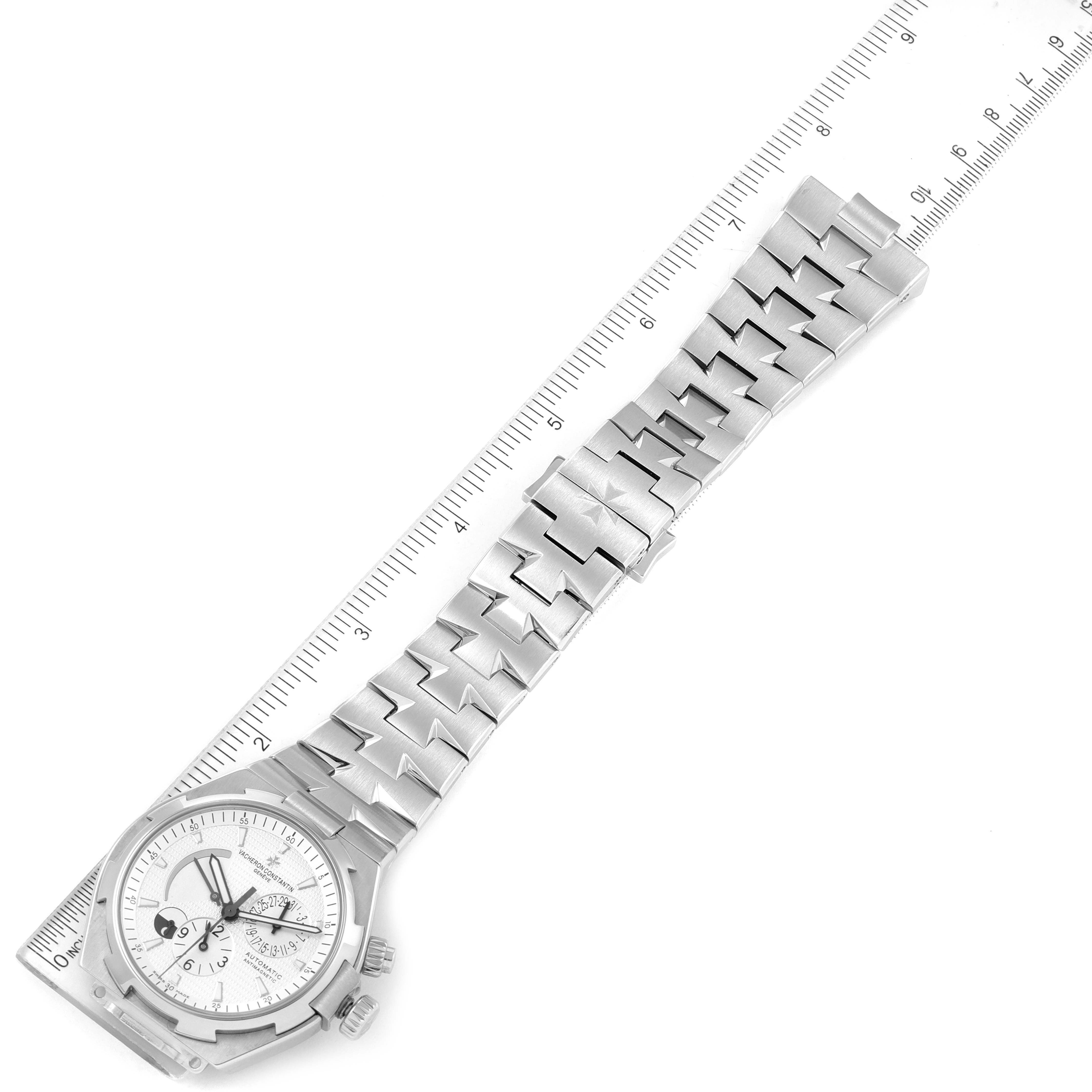 This image shows the Vacheron Constantin Overseas 47450/B01A-9226 Men's Stainless Steel Silver Dial 47450/B01A-9226 Men's Stainless Steel Silver Dial model watch lying flat with a focus on its face and bracelet alongside a ruler.