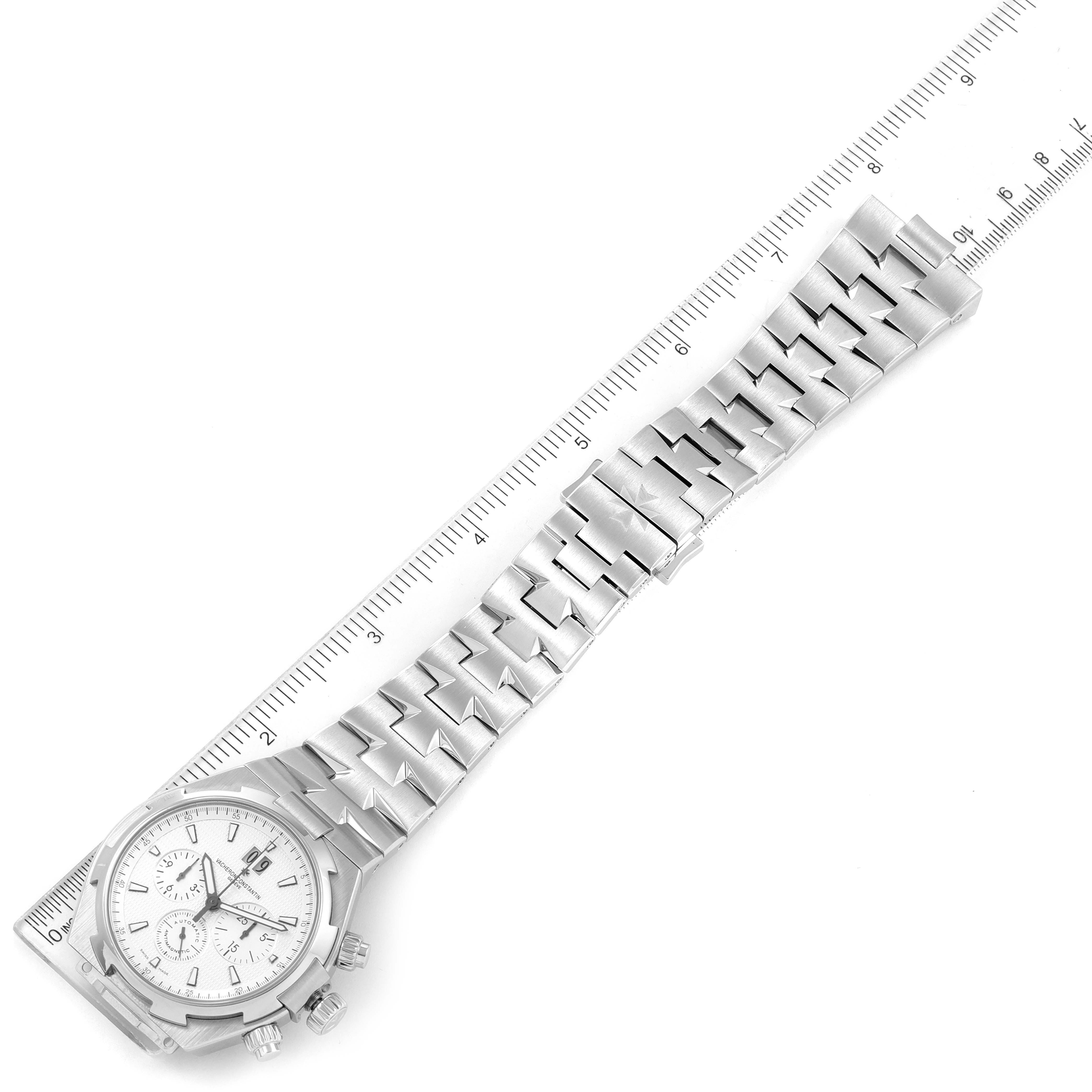The image shows a Vacheron Constantin Overseas 49150/B01A-9095 Men's Stainless Steel Silver Dial 49150/B01A-9095 Men's Stainless Steel Silver Dial model watch laid flat, with a ruler for scale, displaying the face and full metal bracelet.