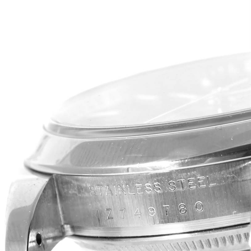 The image shows the side view of a Rolex Date 115200 Men's Stainless Steel Black Dial 115200 Men's Stainless Steel Black Dial model watch, highlighting the stainless steel case and serial number.