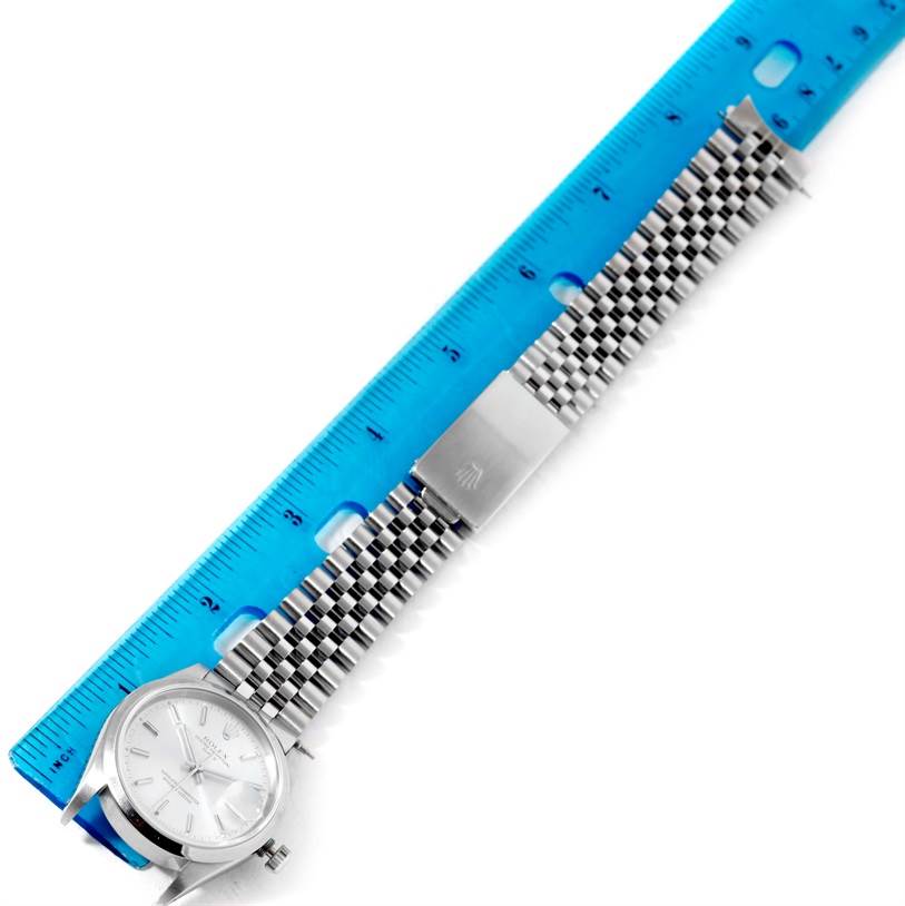 The image shows a Rolex Date 15200 Men's Stainless Steel Silver Dial 15200 Men's Stainless Steel Silver Dial model watch from the top, with its face, bracelet, and clasp next to a blue ruler.