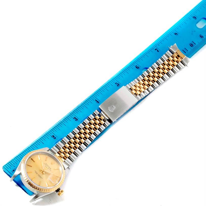The image shows a Rolex Date 15223 Men's Steel and Gold (two tone) Champagne Dial 15223 Men's Steel and Gold (two tone) Champagne Dial model watch laid flat next to a blue ruler, displaying its gold dial, bezel, and two-tone bracelet.