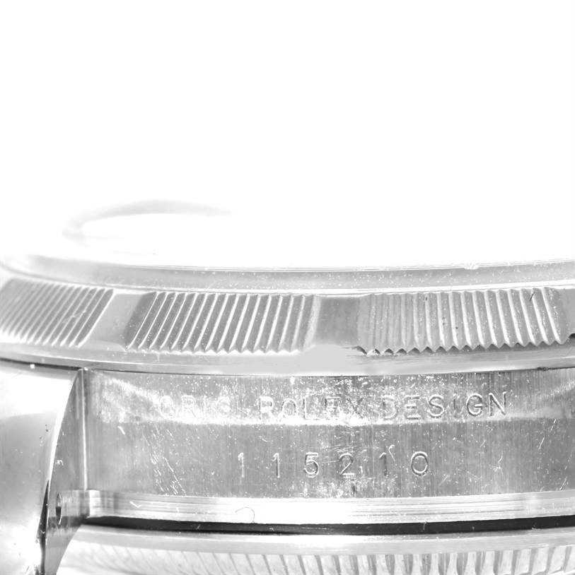 The image shows a close-up side view of the bezel and case of a Rolex Date 115200 Men's Stainless Steel Black Dial 115200 Men's Stainless Steel Black Dial model watch, with visible engravings.