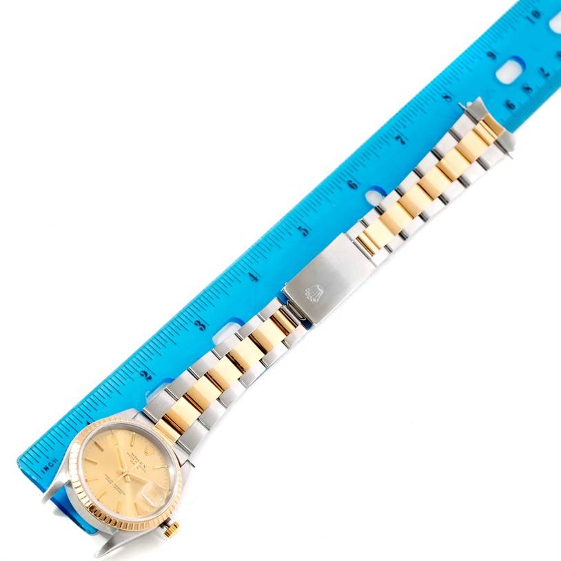 The Rolex Date 15223 Men's Steel and Gold (two tone) Champagne Dial 15223 Men's Steel and Gold (two tone) Champagne Dial watch is shown laid flat next to a blue ruler, displaying the band and face from a top-down angle.