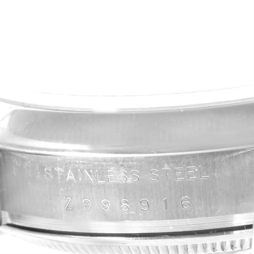 The image shows a close-up side view of a stainless steel Rolex Date 115200SRO Men's Stainless Steel White Dial 115200SRO Men's Stainless Steel White Dial model, focusing on the engraved serial number.