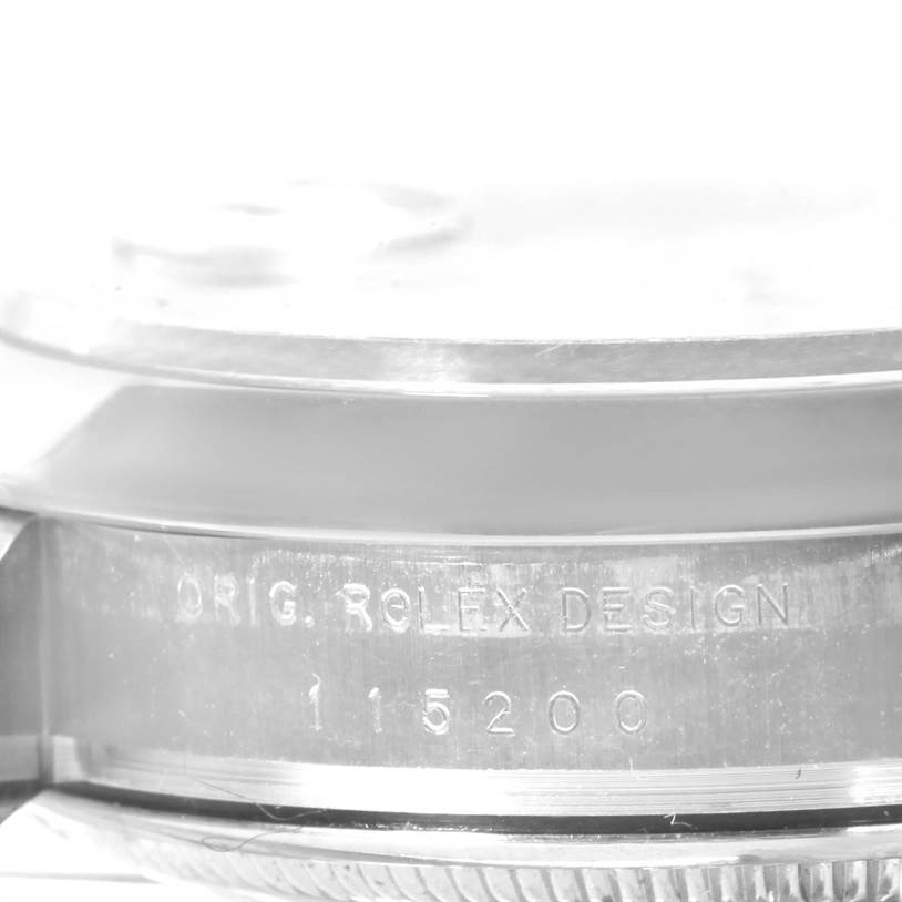 The image shows a side view of a Rolex Date 115200SRO Men's Stainless Steel White Dial 115200SRO Men's Stainless Steel White Dial model watch, focusing on the engraved text on the case.
