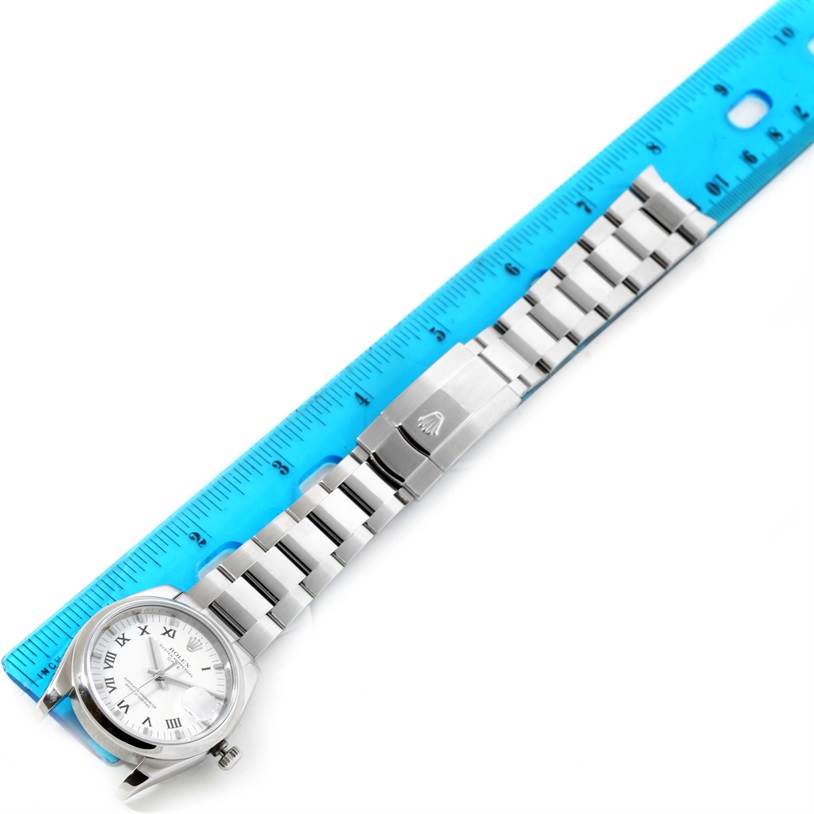 The image shows a Rolex Date 115200SRO Men's Stainless Steel White Dial 115200SRO Men's Stainless Steel White Dial model watch laid flat with its full length and metal bracelet visible, next to a blue ruler.