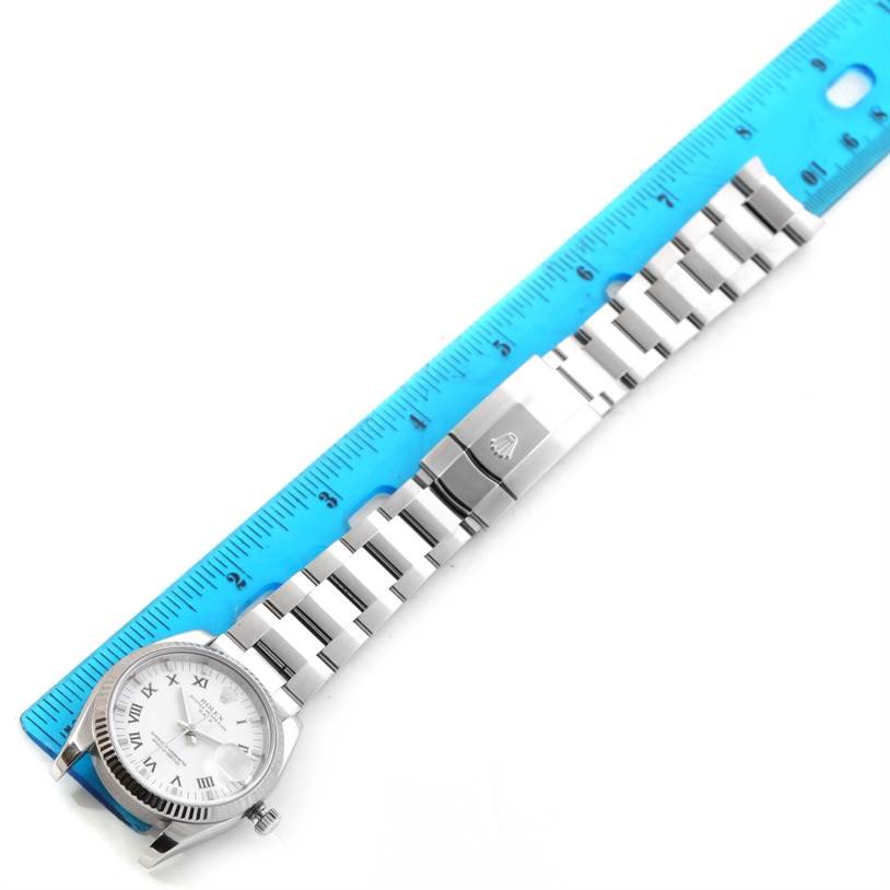 The Rolex Date 115234WRO Men's Stainless Steel White Dial 115234WRO Men's Stainless Steel White Dial model watch is displayed with its band fully extended next to a ruler for measurement.