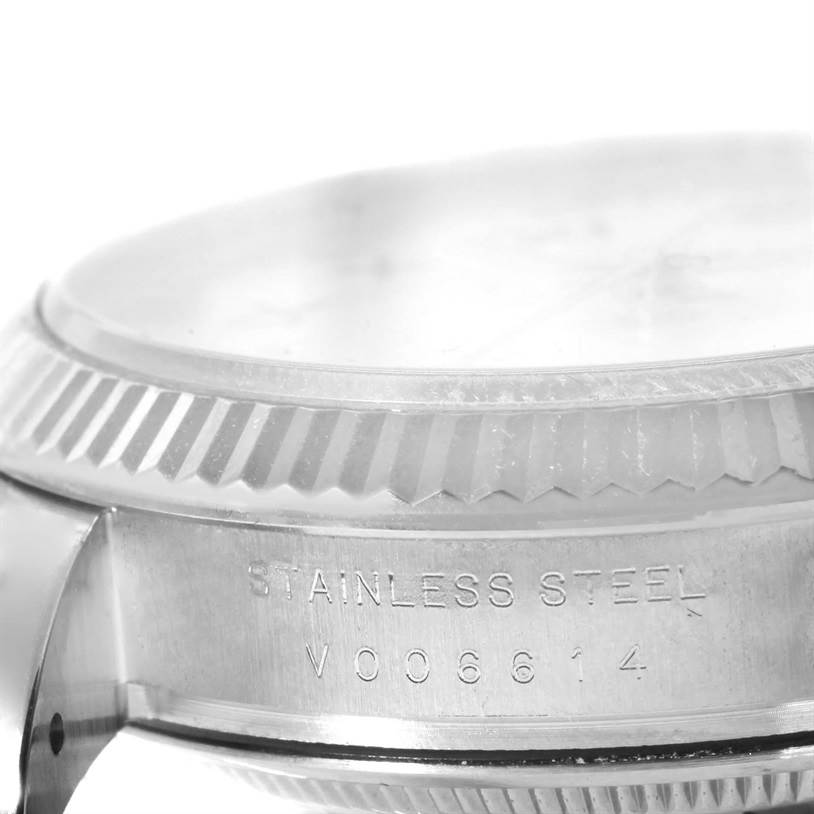 This image shows a close-up side angle of a stainless steel Rolex Date 115234WRO Men's Stainless Steel White Dial 115234WRO Men's Stainless Steel White Dial watch, highlighting its bezel and engraved serial numbers.