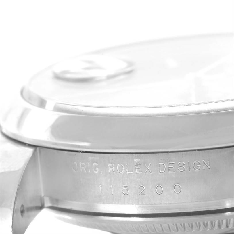 This image shows a close-up side view of the Rolex Date 115200 Men's Stainless Steel Blue Dial 115200 Men's Stainless Steel Blue Dial model, focusing on the bezel and the case with the engraved model number.