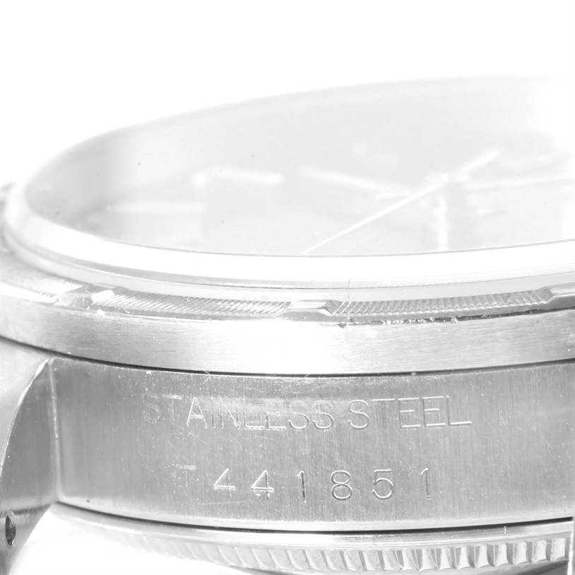 The image shows a close-up, side view of a stainless steel Rolex Date 15210 Men's Stainless Steel Blue Dial 15210 Men's Stainless Steel Blue Dial model, highlighting the bezel and case with its serial number.