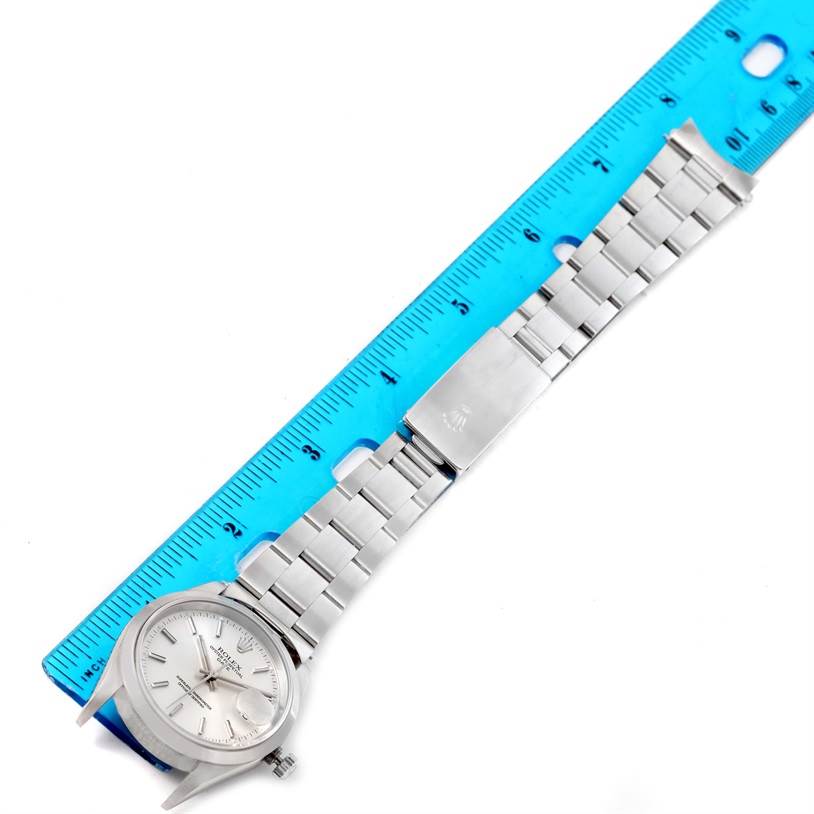 A Rolex Date 15200 Men's Stainless Steel Black Dial 15200 Men's Stainless Steel Black Dial model watch is shown from a top-down angle with the bracelet extended beside a blue ruler.