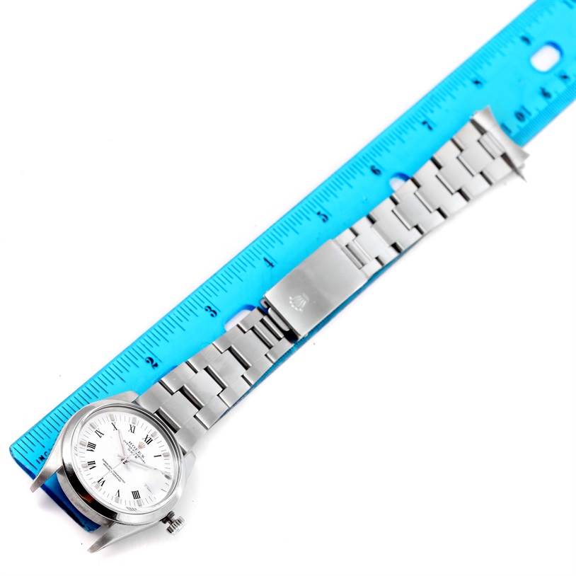 The Rolex Date 15000 Men's Stainless Steel White Dial 15000 Men's Stainless Steel White Dial model watch is shown laid flat with the dial, bracelet, and clasp visible next to a blue ruler.