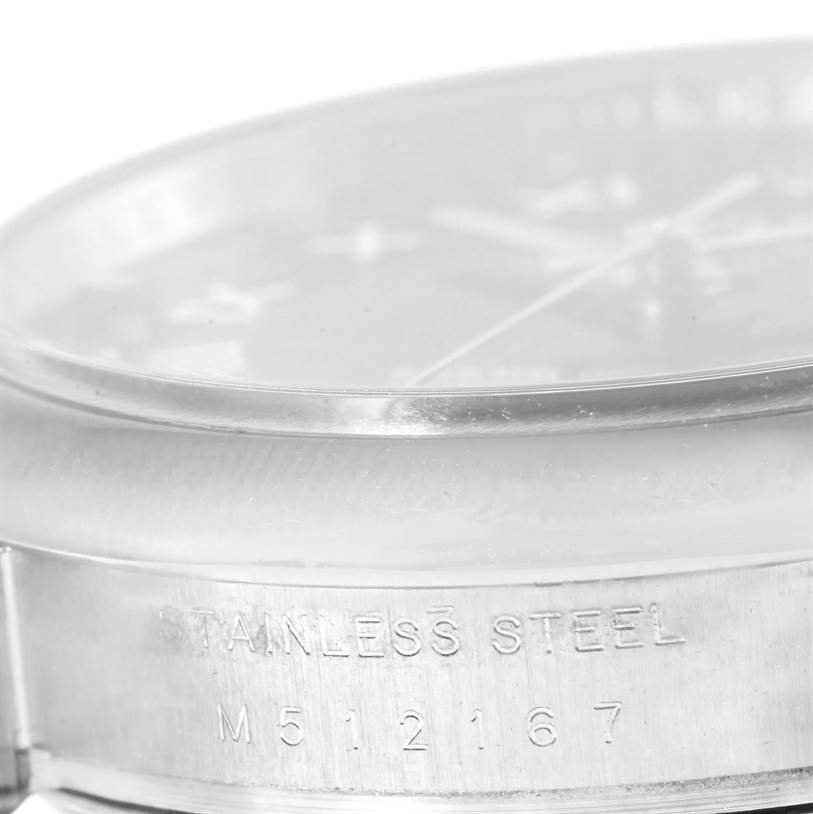 The image shows a close-up of the side view of the case of a Rolex Date 115200 Men's Stainless Steel Black Dial 115200 Men's Stainless Steel Black Dial model watch, displaying "STAINLESS STEEL" and the serial number.