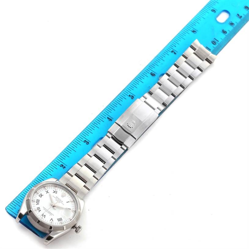 The image shows a Rolex Date 115210 Men's Stainless Steel White Dial 115210 Men's Stainless Steel White Dial model watch laid flat next to a blue ruler, highlighting the watch face and metal bracelet.