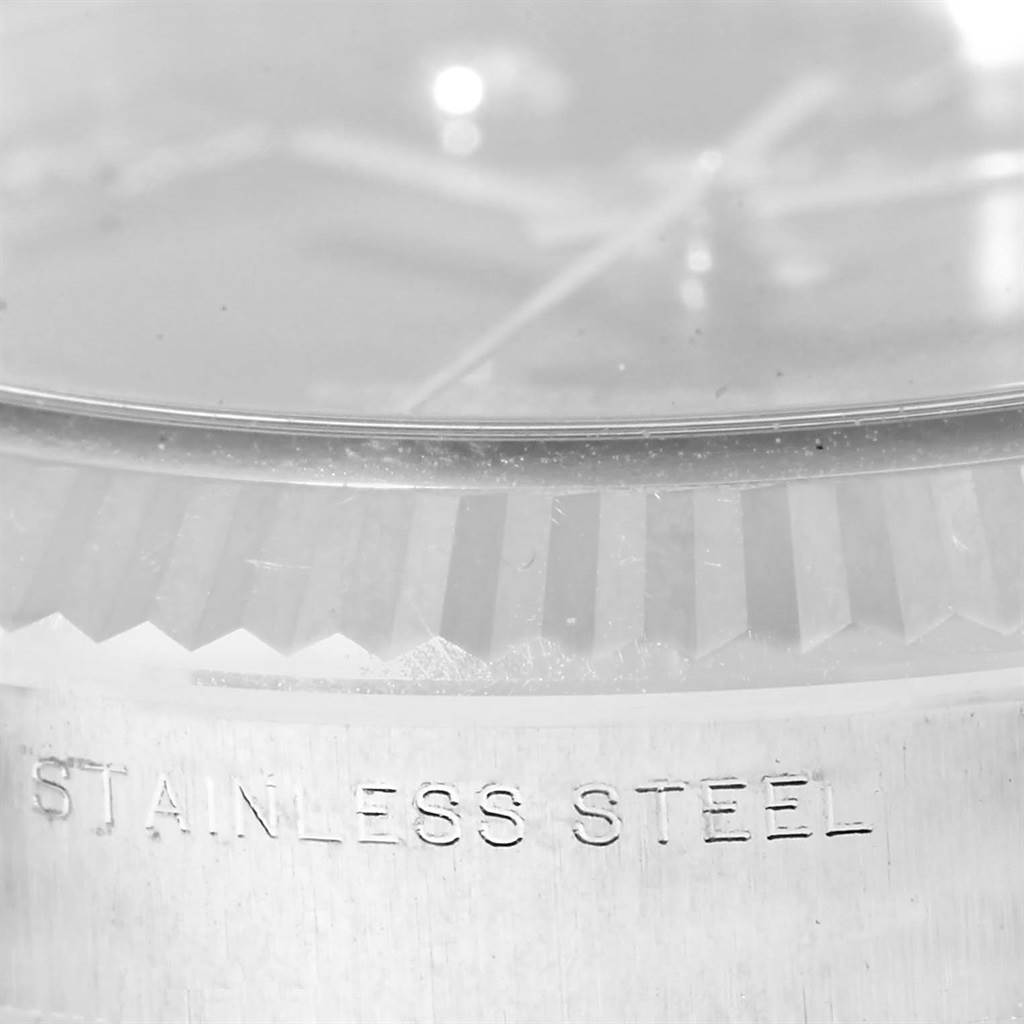 This close-up image of a Rolex Date 115234 Men's Stainless Steel Black Dial 115234 Men's Stainless Steel Black Dial watch shows the fluted bezel and part of the stainless steel case.