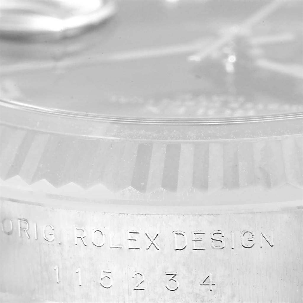 The image shows a close-up of the case and bezel of a Rolex Date 115234 Men's Stainless Steel Black Dial 115234 Men's Stainless Steel Black Dial model, featuring the model's serial number engraving.