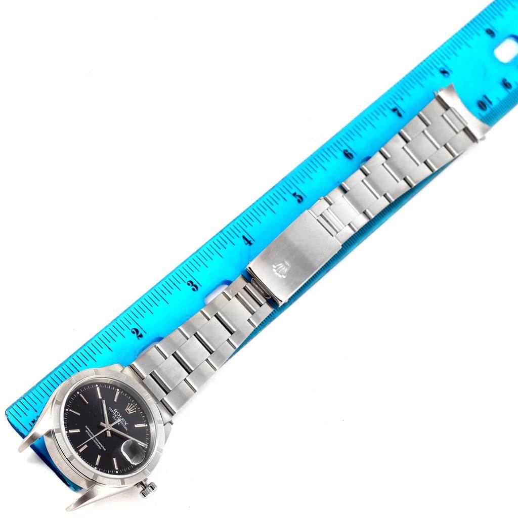 This image shows a Rolex Date 15210 Men's Stainless Steel Black Dial 15210 Men's Stainless Steel Black Dial model watch laid flat against a ruler, displaying the entire watch band and face from a top-down angle.