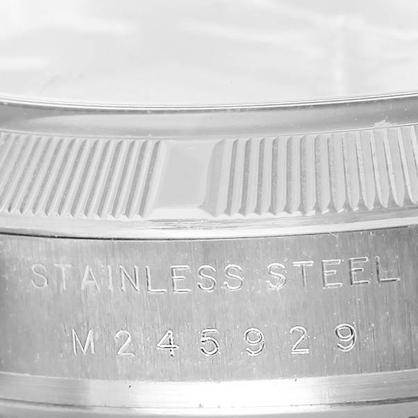 The image shows a close-up of the case side and fluted bezel of a Rolex Date 115210 Men's Stainless Steel Blue Dial 115210 Men's Stainless Steel Blue Dial model watch, highlighting the "Stainless Steel" engraving with a serial number.