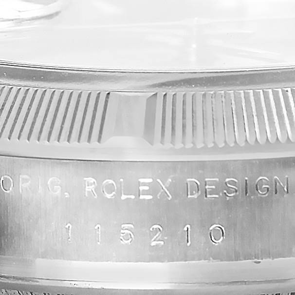 The image shows a close-up of the engraved bezel and case side of a Rolex Date 115210 Men's Stainless Steel Blue Dial 115210 Men's Stainless Steel Blue Dial model watch.