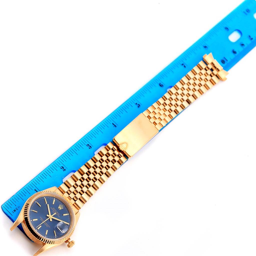 The Rolex Date 15238 Men's Yellow Gold Blue Dial 15238 Men's Yellow Gold Blue Dial watch is shown at an overhead angle with its face, crown, and bracelet visible next to a blue ruler.