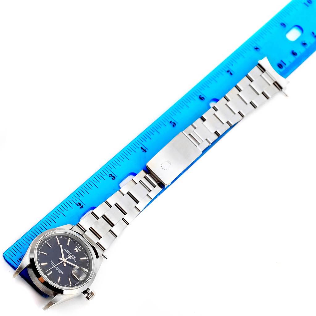 The Rolex Date 15200 Men's Stainless Steel Black Dial 15200 Men's Stainless Steel Black Dial model watch is shown from an overhead angle, displaying the face, bezel, bracelet, and clasp next to a ruler.