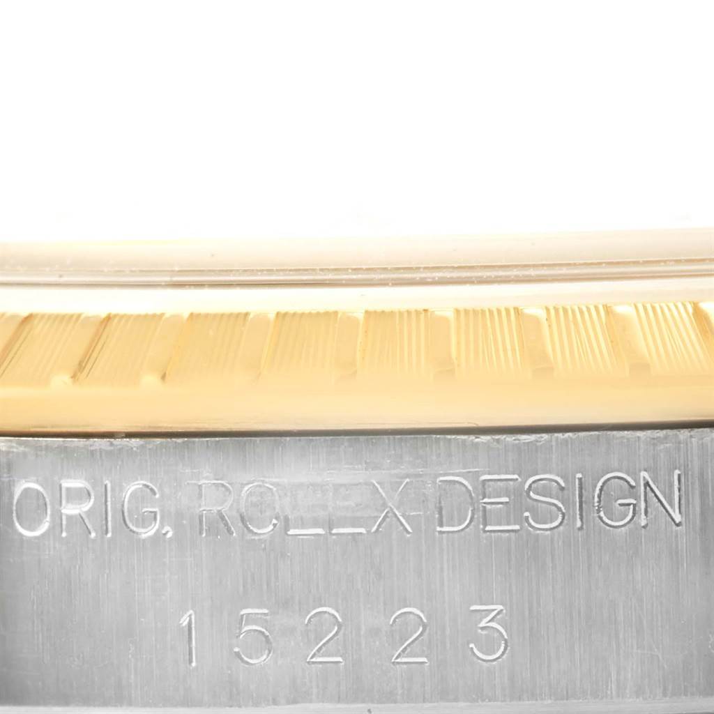 This image shows a close-up of the side of a Rolex Date 15223 Men's Steel and Gold (two tone) Silver Dial 15223 Men's Steel and Gold (two tone) Silver Dial model watch, featuring part of the bezel and watch case with engraved text.