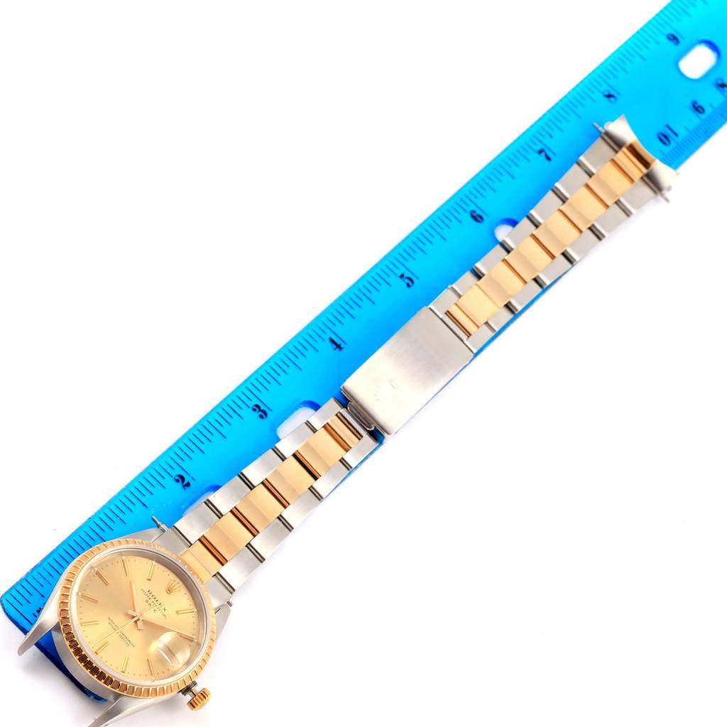 The image shows a Rolex Date 15223 Men's Steel and Gold (two tone) Champagne Dial 15223 Men's Steel and Gold (two tone) Champagne Dial model watch laid flat next to a ruler, displaying the face, band, and clasp.