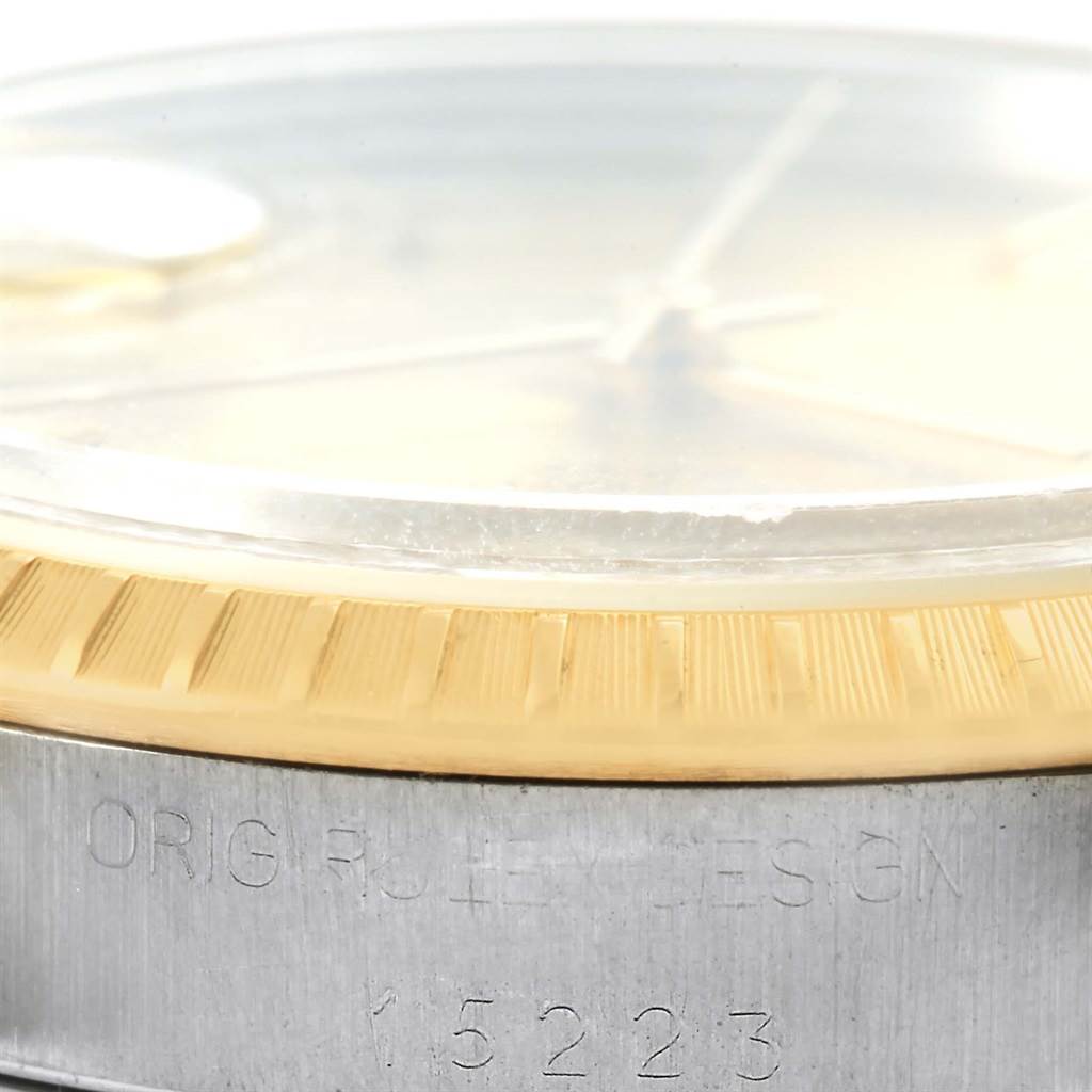 The image shows a close-up angle of the bezel, crystal, and part of the case with engraving on a Rolex Date 15223 Men's Steel and Gold (two tone) Champagne Dial 15223 Men's Steel and Gold (two tone) Champagne Dial model watch.