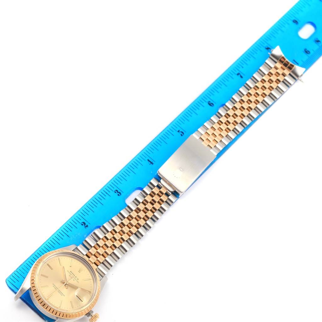 The image shows a top-down view of a Rolex Date 15053 Men's Steel and Gold (two tone) Champagne Dial 15053 Men's Steel and Gold (two tone) Champagne Dial watch with a ruler, highlighting the face and the two-tone bracelet.