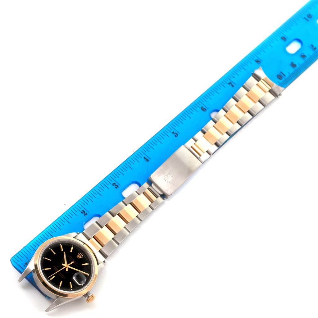The image shows a top view of a Rolex Date 15203 Men's Steel and Gold (two tone) Black Dial 15203 Men's Steel and Gold (two tone) Black Dial model watch alongside a blue ruler for scale.