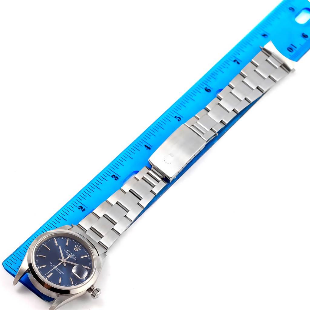 The Rolex Date 15200 Men's Stainless Steel Blue Dial 15200 Men's Stainless Steel Blue Dial model watch is shown from an overhead angle, displaying the face, crown, and metal bracelet, which is measured alongside a blue ruler.