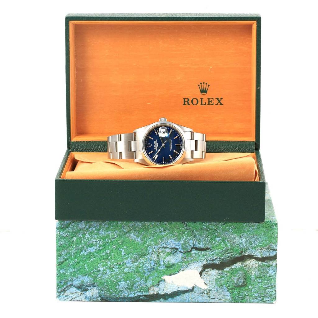 The Rolex Date 15200 Men's Stainless Steel Blue Dial 15200 Men's Stainless Steel Blue Dial watch is shown from the front, placed in an open green and orange box, atop a decorative base.