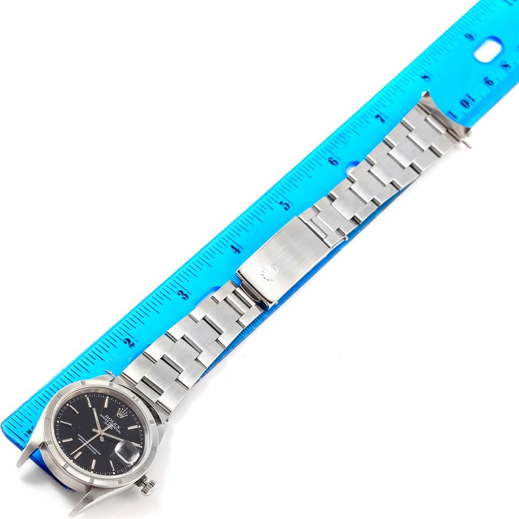 The Rolex Date 15210 Men's Stainless Steel Black Dial 15210 Men's Stainless Steel Black Dial model watch is shown flat, full-length with a focus on the bracelet and clasp beside a blue ruler.