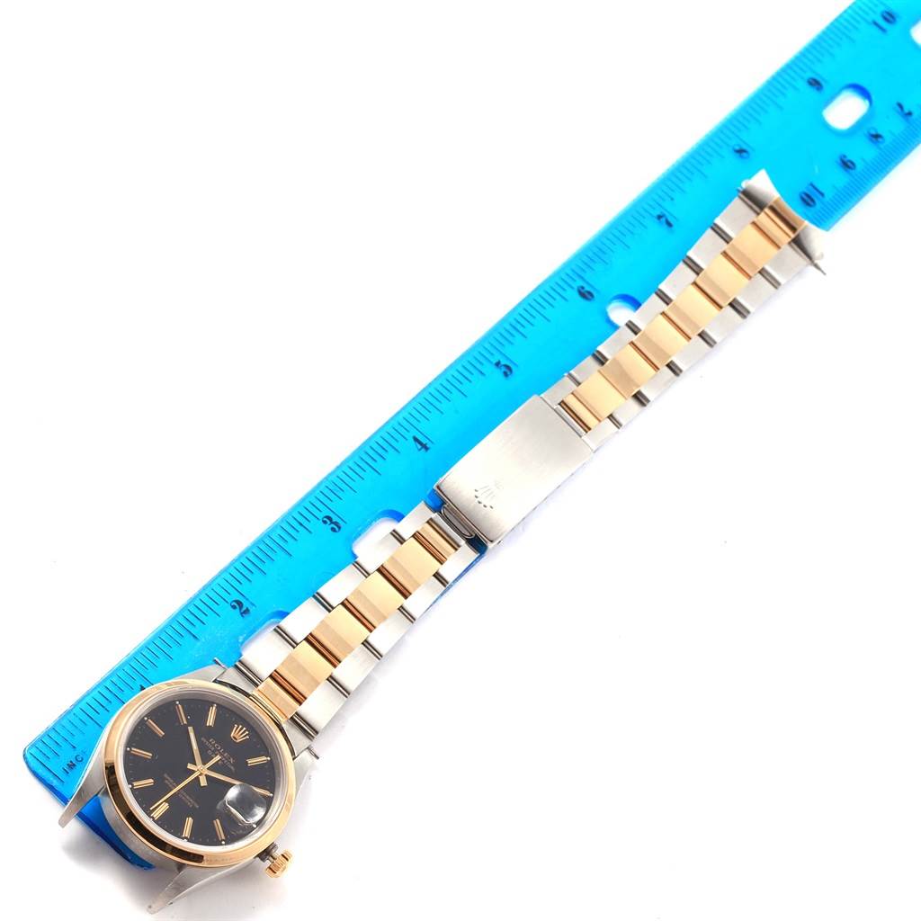 The Rolex Date 15203 Men's Steel and Gold (two tone) Black Dial 15203 Men's Steel and Gold (two tone) Black Dial model watch is shown at an angled top-down view alongside a blue ruler, highlighting the watch face and band.