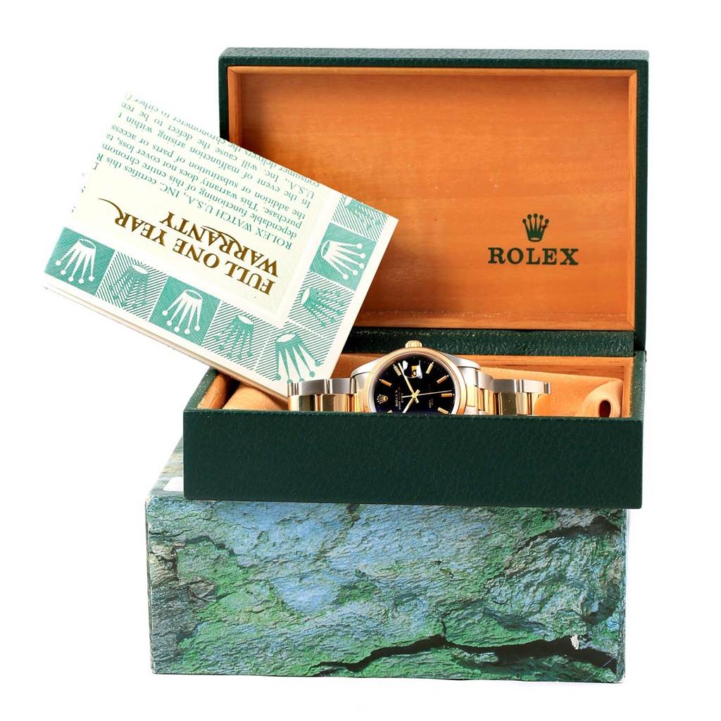 The image shows a Rolex Date 15203 Men's Steel and Gold (two tone) Black Dial 15203 Men's Steel and Gold (two tone) Black Dial model watch partially inside an open box with a warranty card propped up inside the box.