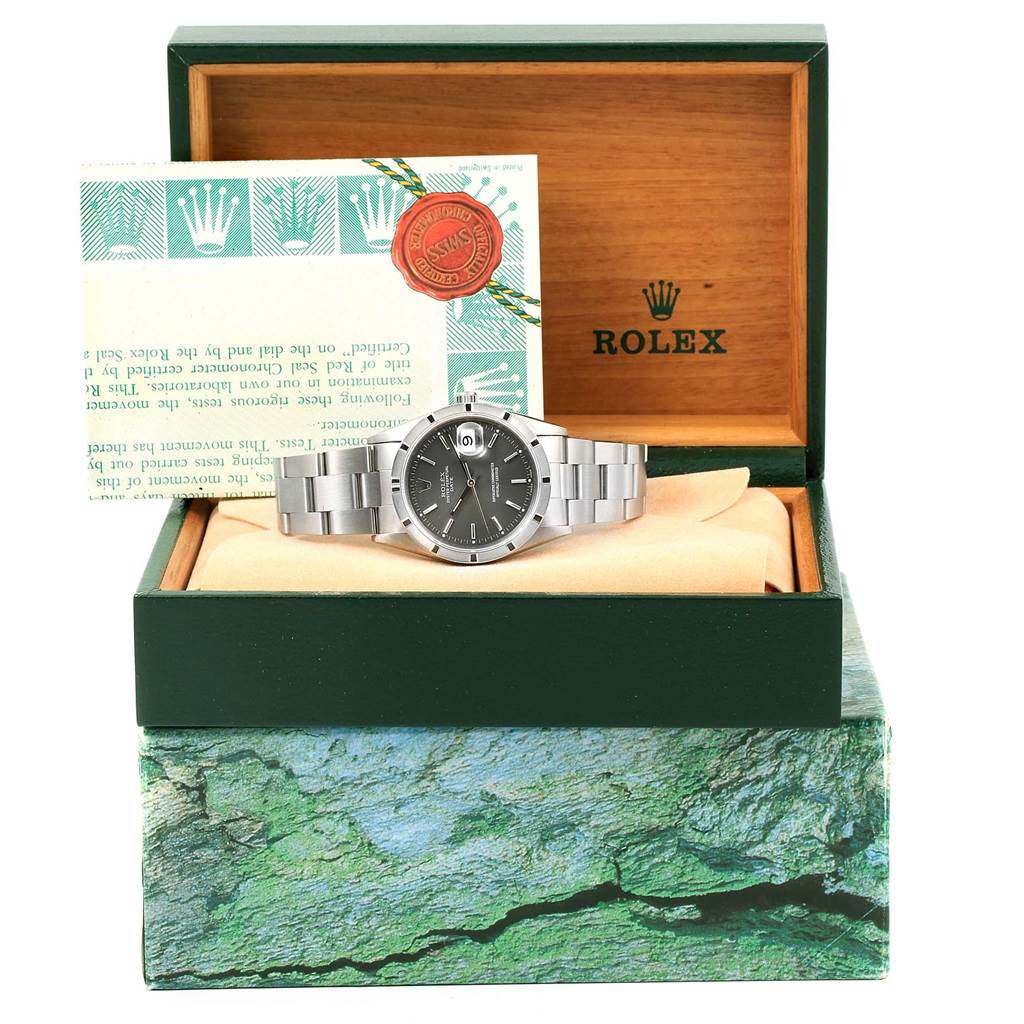 The Rolex Date 15210 Men's Stainless Steel Grey Dial 15210 Men's Stainless Steel Grey Dial model watch is displayed in its open box, with accompanying paperwork visible behind it.