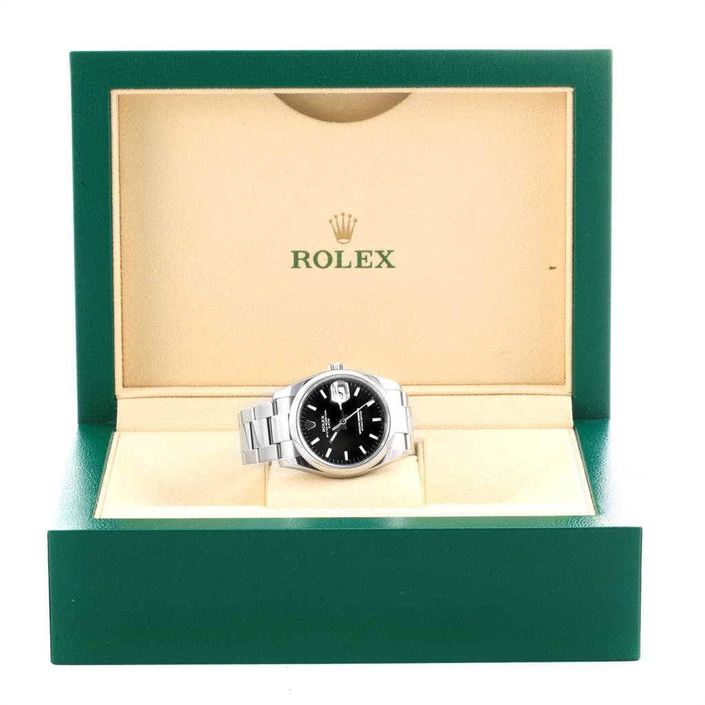 The Rolex Date 115200 Men's Stainless Steel Black Dial 115200 Men's Stainless Steel Black Dial model watch is displayed at a front angle in its open green and beige box.