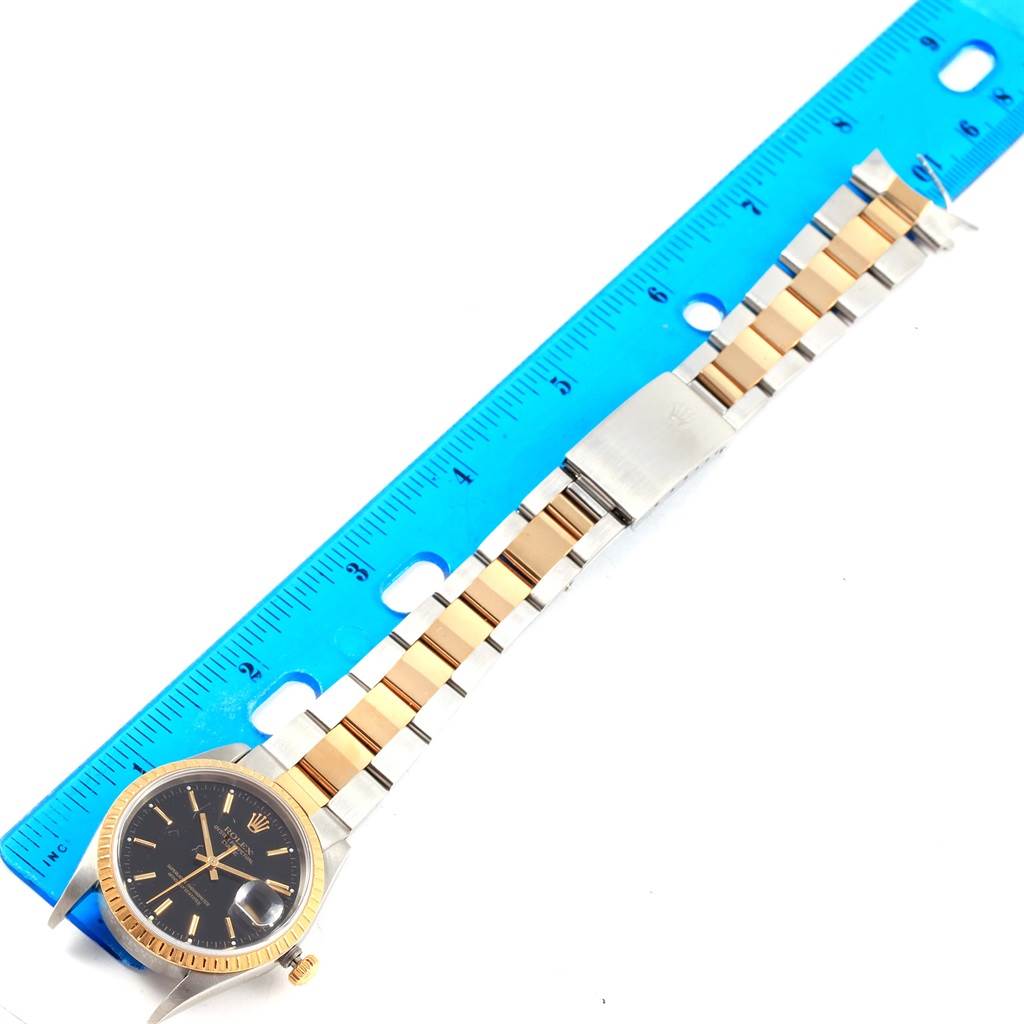 The Rolex Date 15223 Men's Steel and Gold (two tone) Black Dial 15223 Men's Steel and Gold (two tone) Black Dial watch is shown laid flat next to a ruler, highlighting the face, bezel, bracelet, and clasp from a top-down angle.