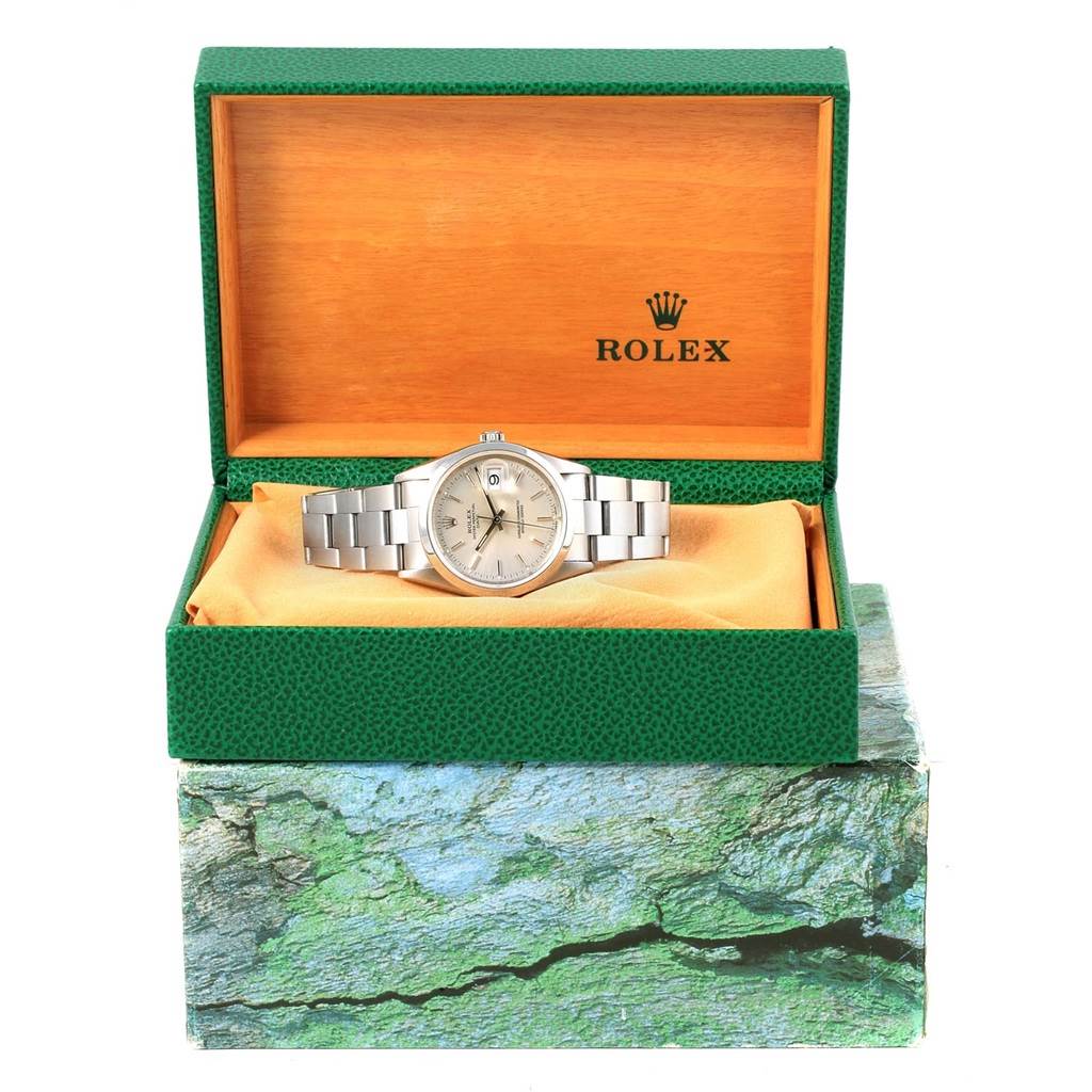 The Rolex Date 15200 Men's Stainless Steel Silver Dial 15200 Men's Stainless Steel Silver Dial model watch is shown front-facing inside an open green and wooden box on a textured base.