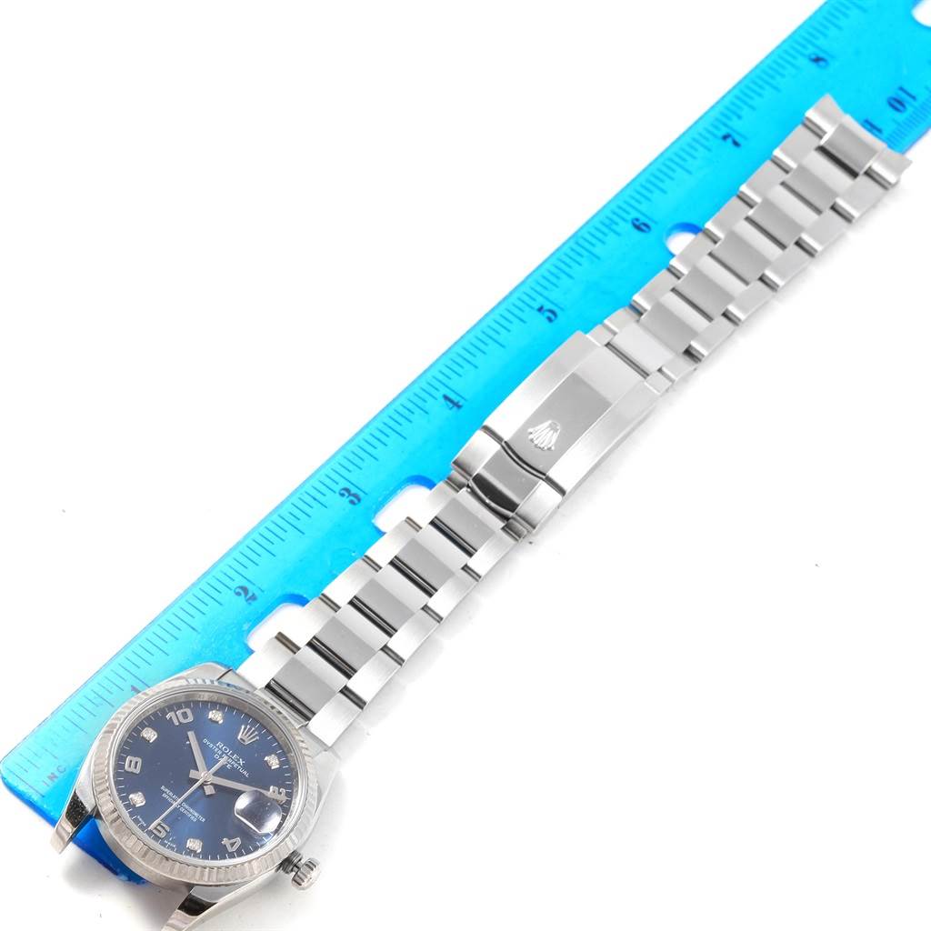 This image shows a Rolex Date 115234 Stainless Steel Blue Dial 115234 Stainless Steel Blue Dial model watch laid flat, highlighting its bracelet and clasp alongside a measuring ruler.