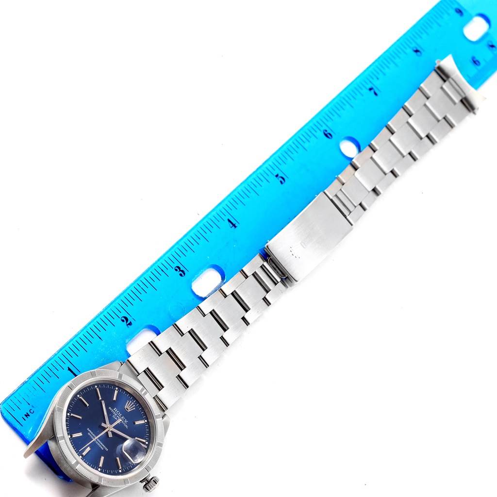 The Rolex Date 15210 Men's Stainless Steel Blue Dial 15210 Men's Stainless Steel Blue Dial watch is displayed flat, showing the face, bezel, crown, and entirety of the metal bracelet next to a blue ruler.