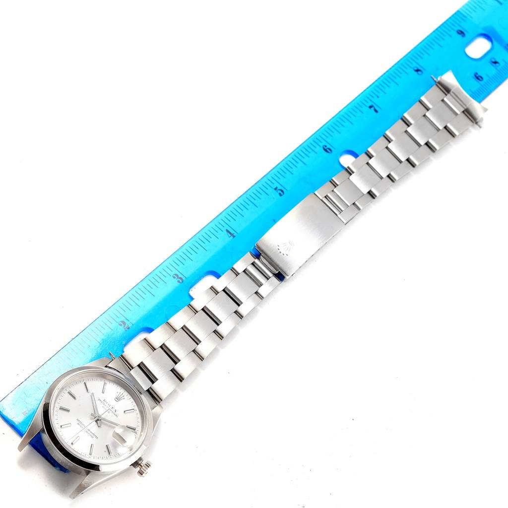 The image shows a Rolex Date 15200 Men's Stainless Steel Silver Dial 15200 Men's Stainless Steel Silver Dial model watch with its bracelet spread out beside a blue ruler for measurement.